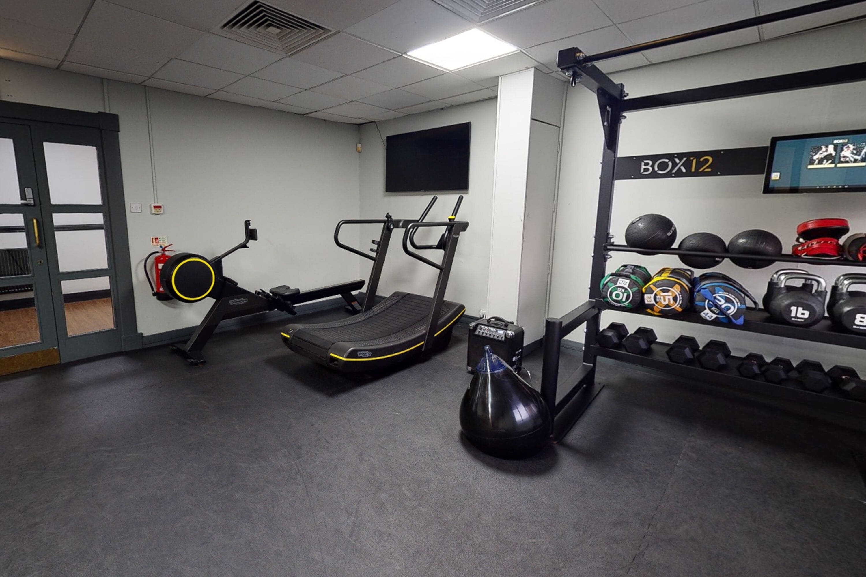 Un gimnasio con cintas de correr, una bicicleta estática y un soporte para pesas con mancuernas y balones medicinales.