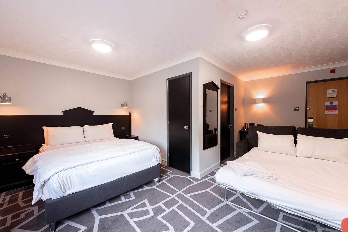A hotel room with two beds, a dark headboard, a patterned carpet, and wall-mounted lights.