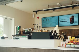 A coffee shop counter with a menu board, coffee machines, and a variety of snacks and condiments.