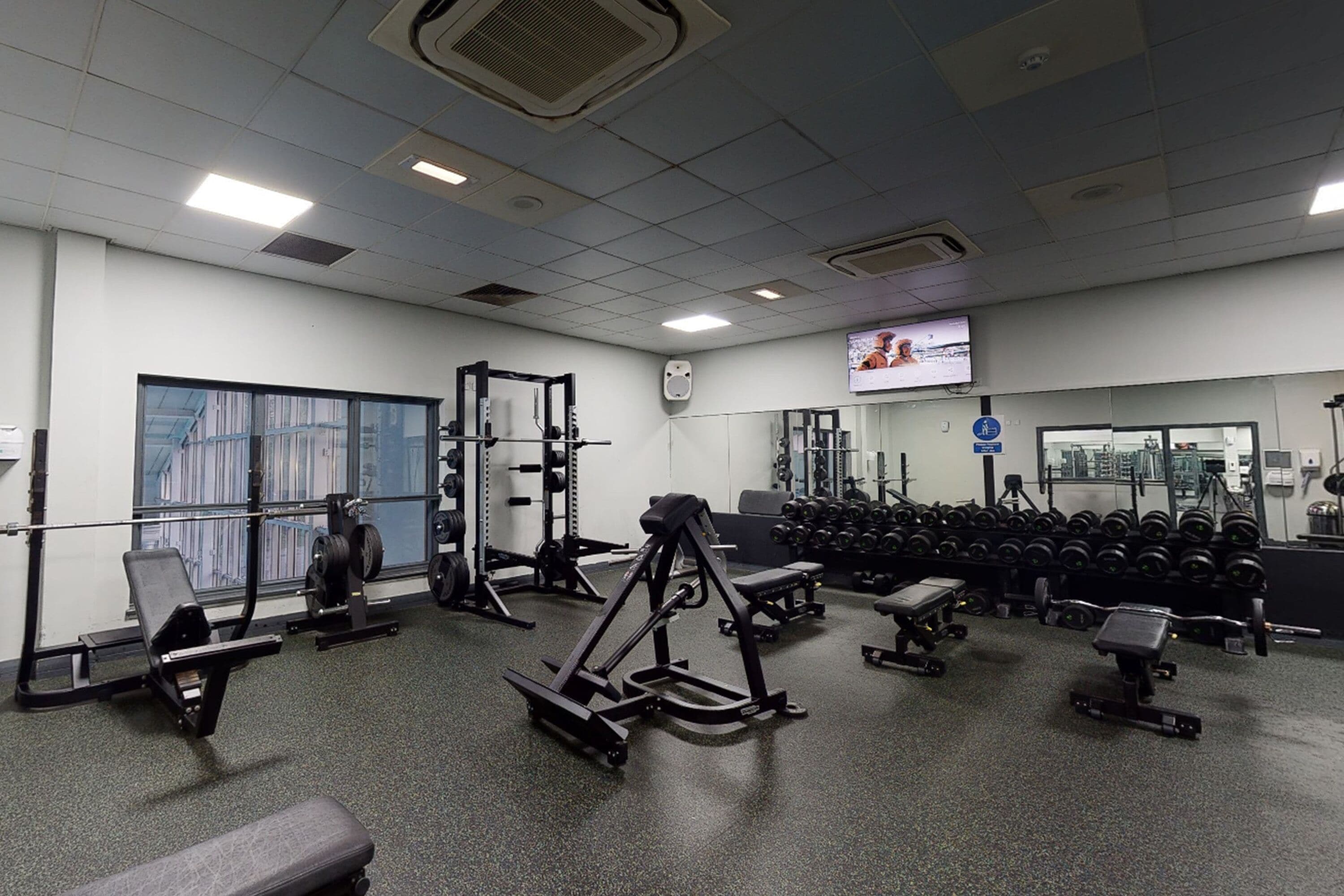 A gym with various exercise equipment, a television on the wall, and a large window.
