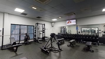 Un gimnasio con diferentes equipos de ejercicio, un televisor en la pared y un ventanal grande.