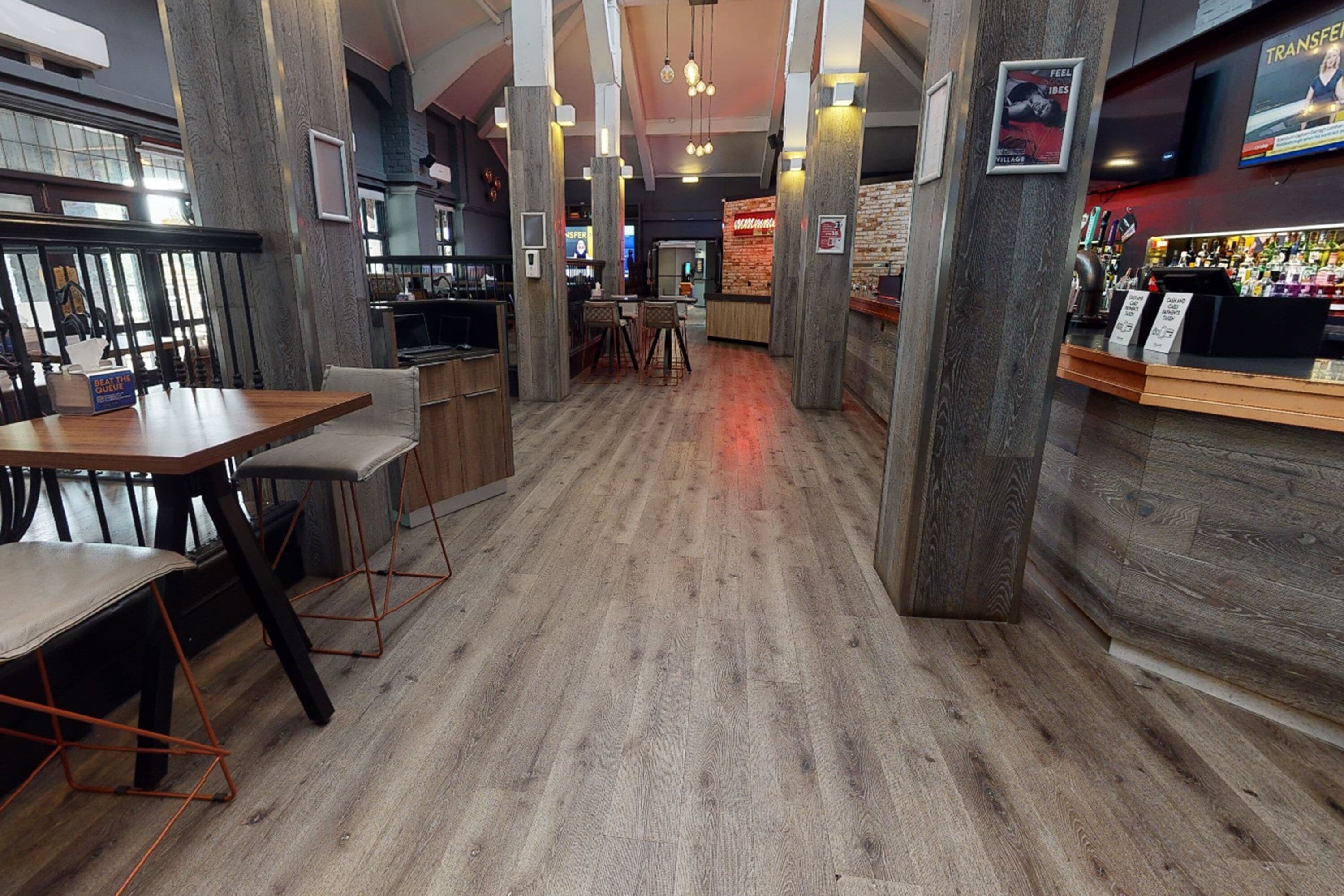 Interior de restaurante con suelo de madera, techos altos y vigas a la vista. Mesas y sillas dispuestas para comer.