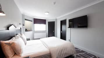 A modern hotel room with a bed, a flat-screen TV mounted on the wall, a window with a view, and a door.