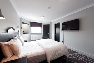 Una habitación de hotel moderna con una cama, un televisor de pantalla plana montado en la pared, una ventana con vistas y una puerta.