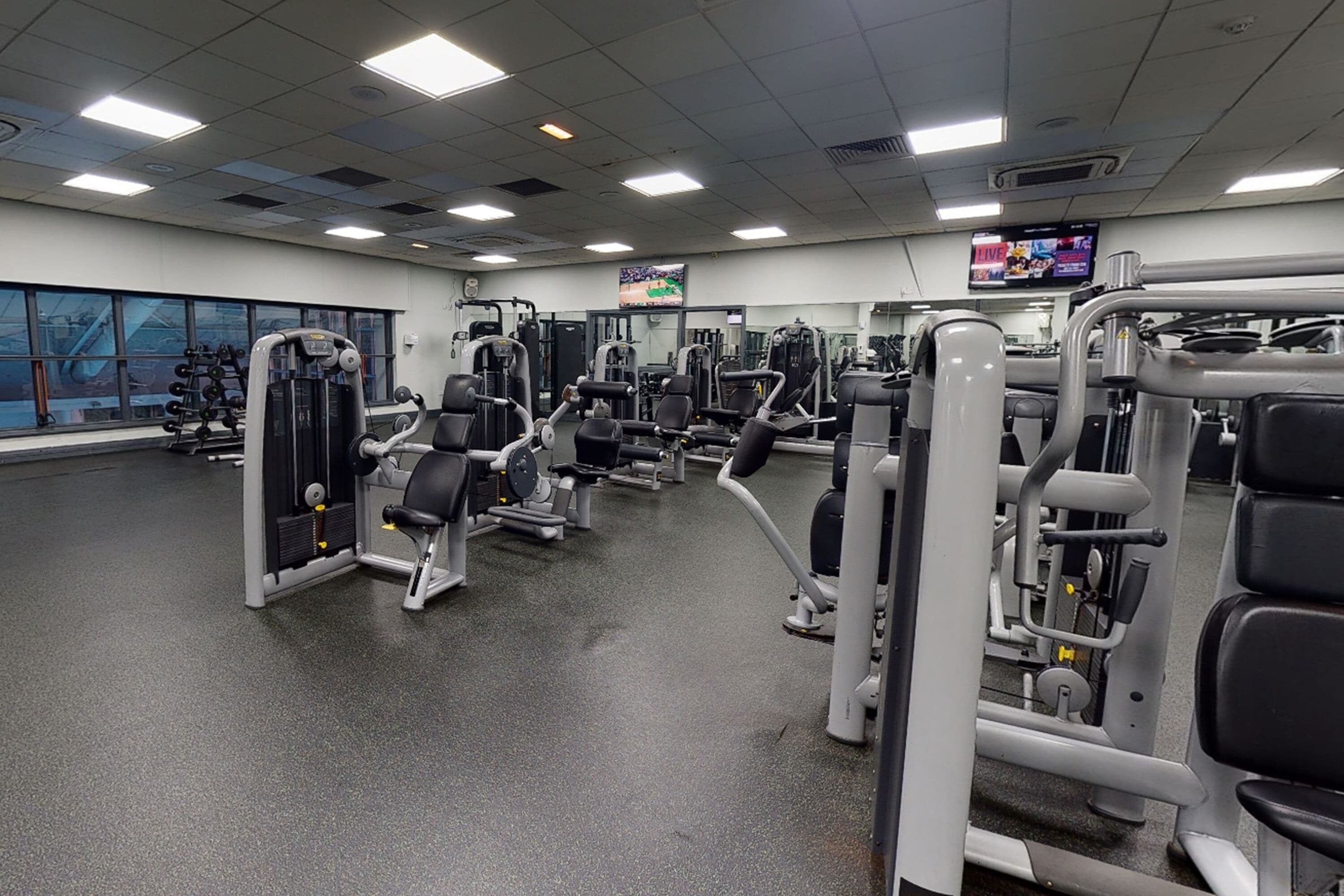 A gym with various exercise machines, a large mirror, and a TV screen.