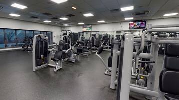 A gym with various exercise machines, a large mirror, and a TV screen.