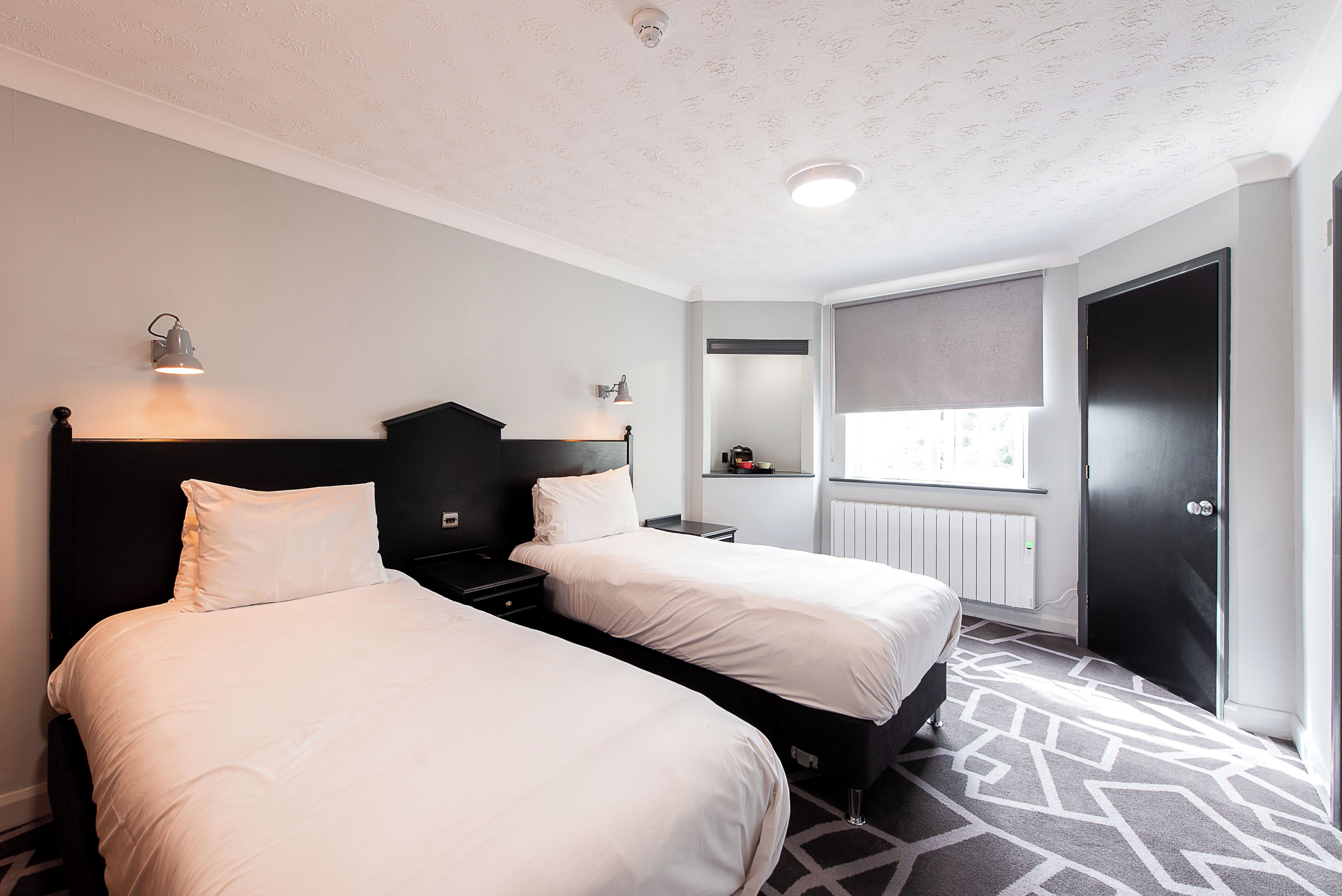 A hotel room with two beds, a window with a view, a radiator, and a door.