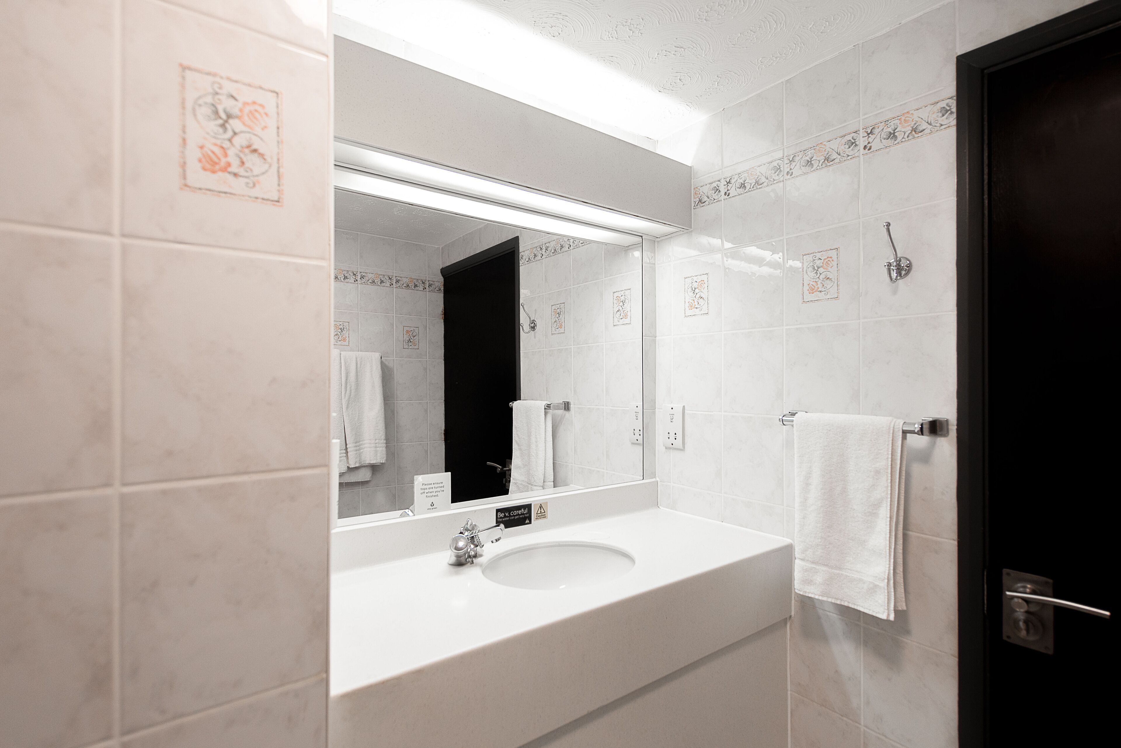 A bathroom with a white sink, a large mirror, and a black door.