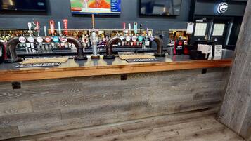 Zona de bar con mostrador de madera, varias grifos de cerveza y una pantalla de televisión arriba.