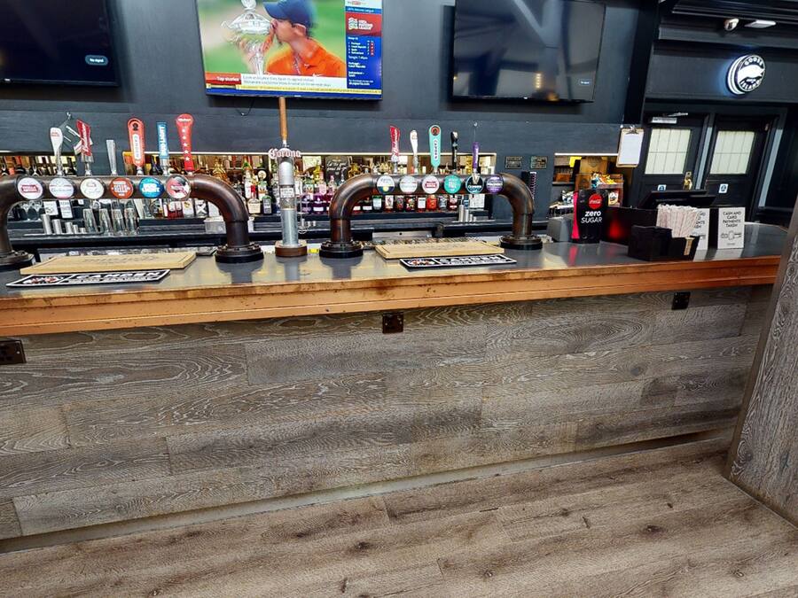 Un espace bar doté d’un comptoir en bois, de plusieurs robinets à bière et d’un écran de télévision placé au-dessus.