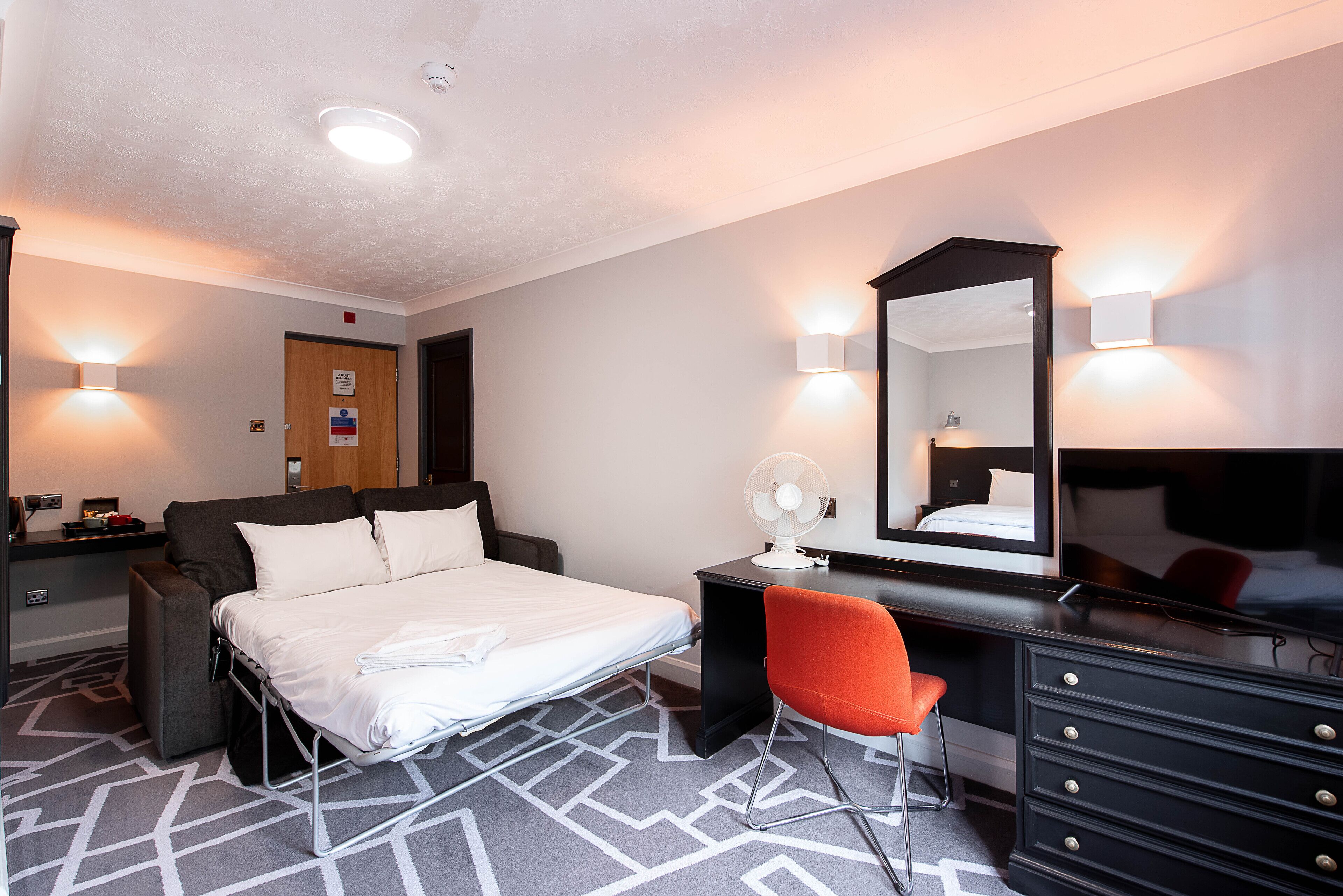A hotel room with a bed, a desk, a chair, a dresser, and a mirror.