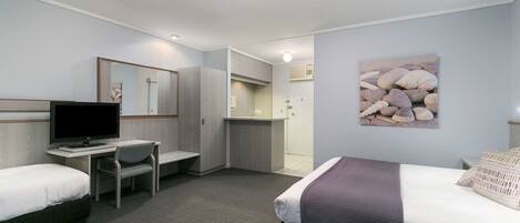 A hotel room with two beds, a desk with a computer, a mirror, and a painting of shells on the wall.