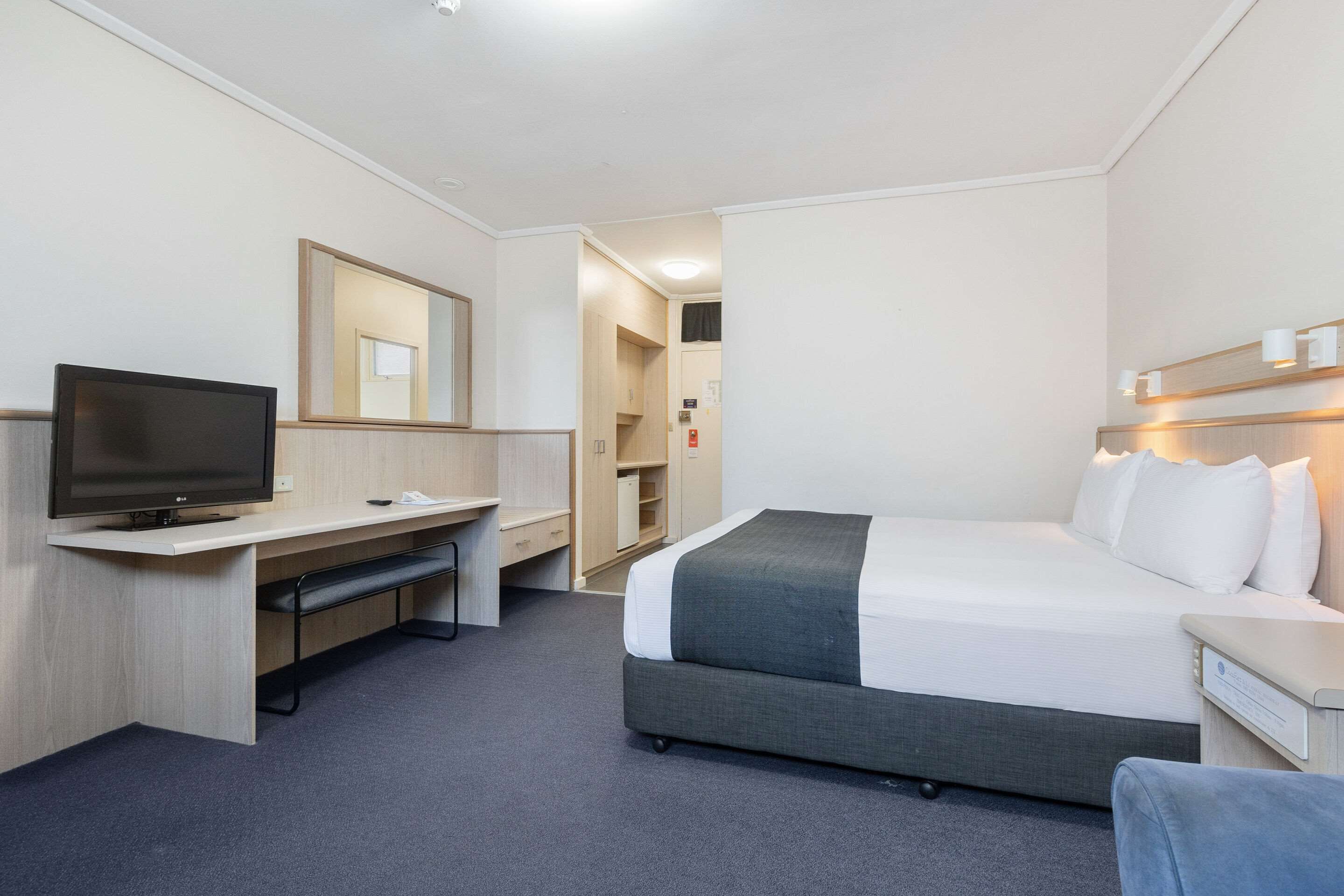 Una habitación de hotel con cama, escritorio, televisor y espejo.
