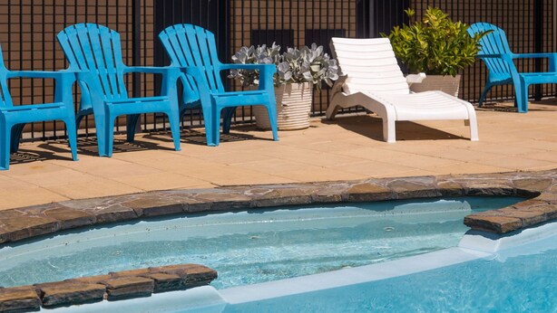 Une piscine entourée de chaises longues bleues et blanches, d’une chaise longue blanche et de plantes en pot.