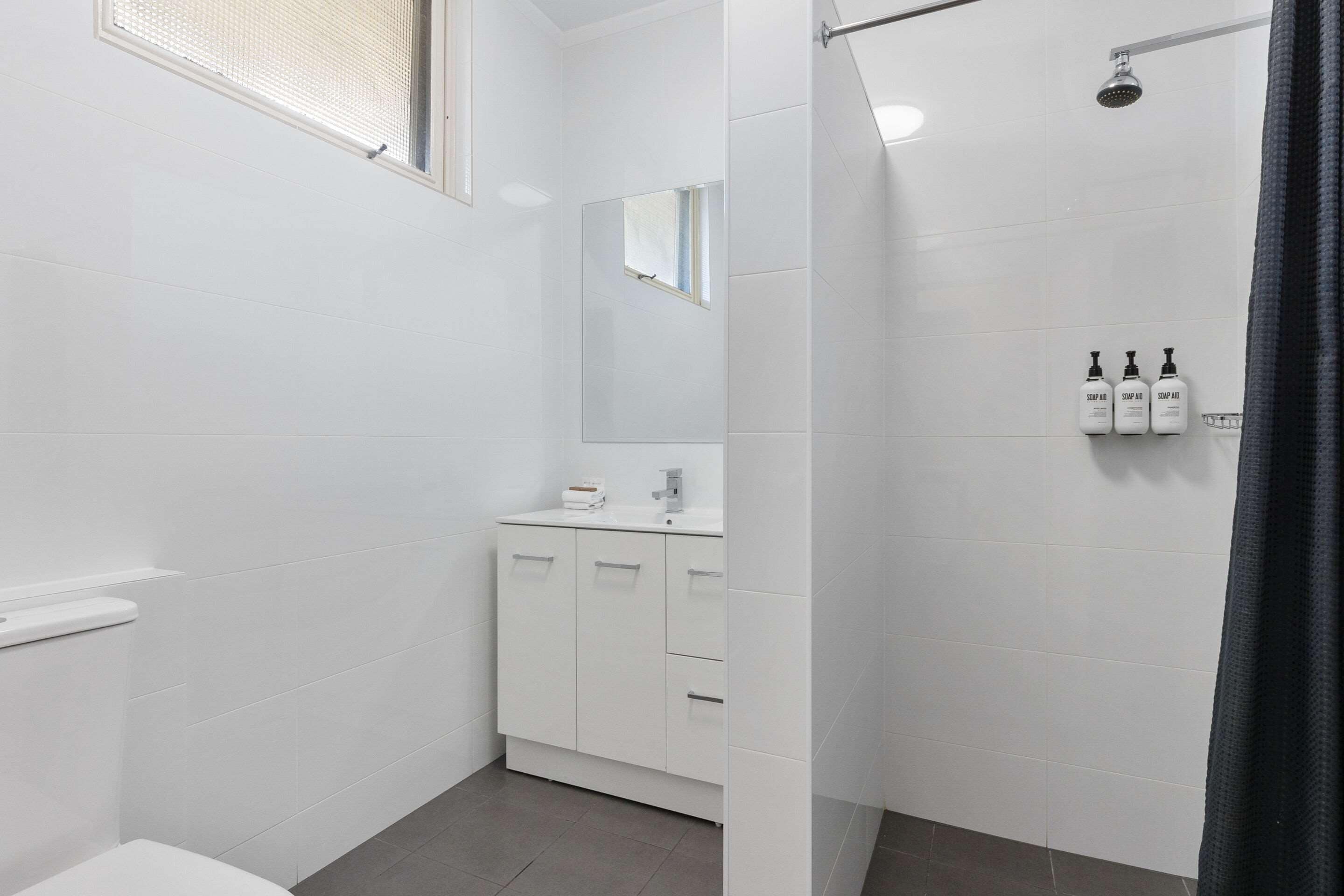 Un baño moderno con azulejos blancos, un inodoro, un lavabo con espejo y una zona de ducha.
