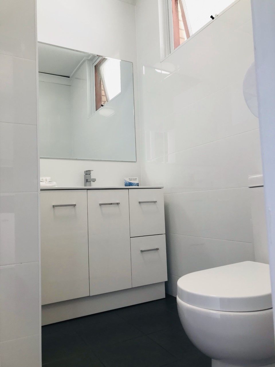 A bathroom with white cabinets, a mirror, and a toilet.
