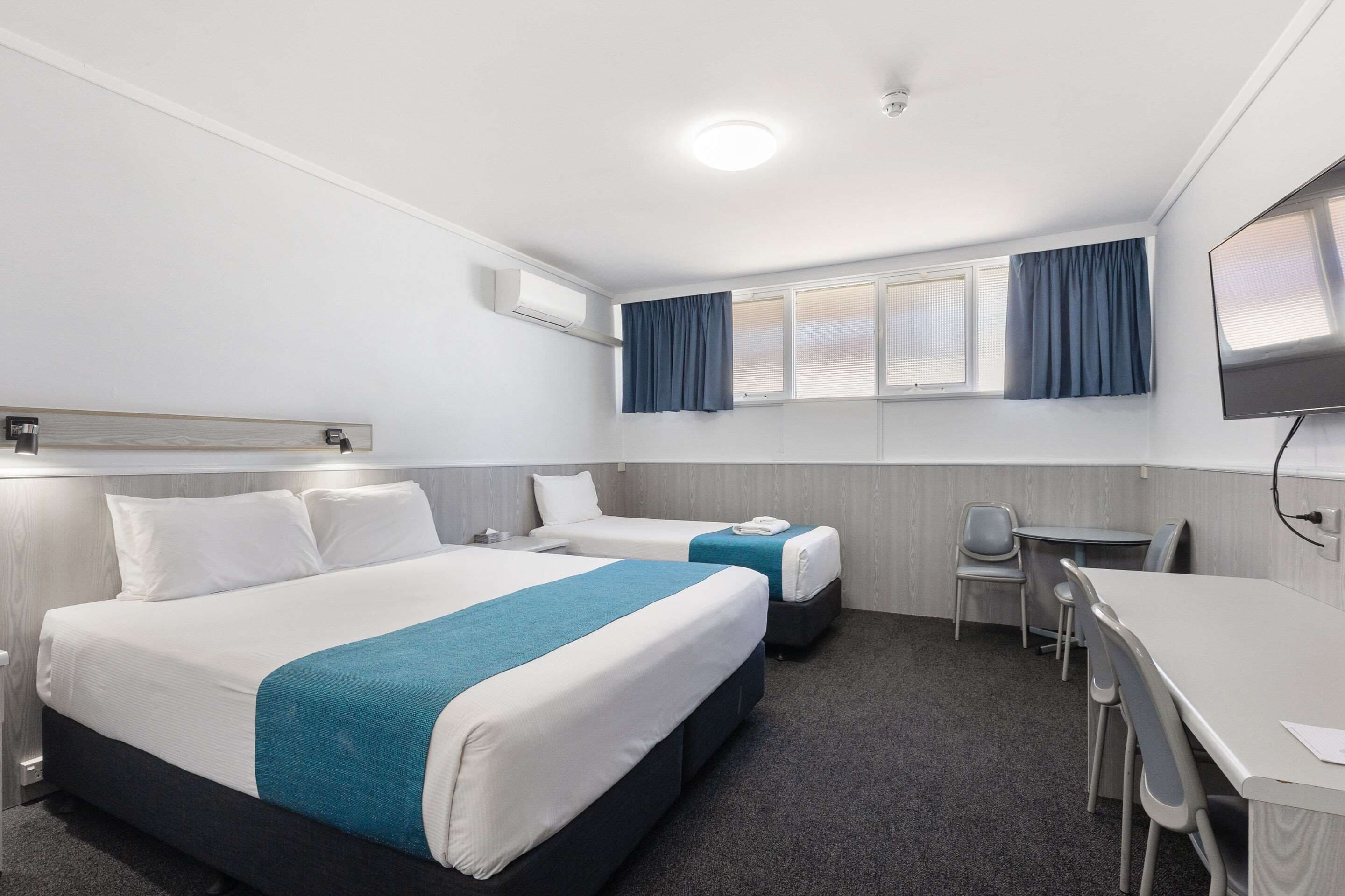 Een hotelkamer met twee bedden, een bureau en een stoel. Er is een televisie aan de muur en een airconditioning boven het bed.