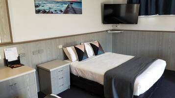 A hotel room with a bed, a nightstand, a TV, and a painting of a sunset over the ocean.