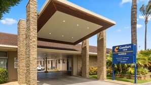 L’entrée d’un hôtel Comfort Inn, avec un espace de stationnement couvert, des piliers en pierre et un panneau indiquant les équipements disponibles, tels qu’une piscine et des cuisines américaines.