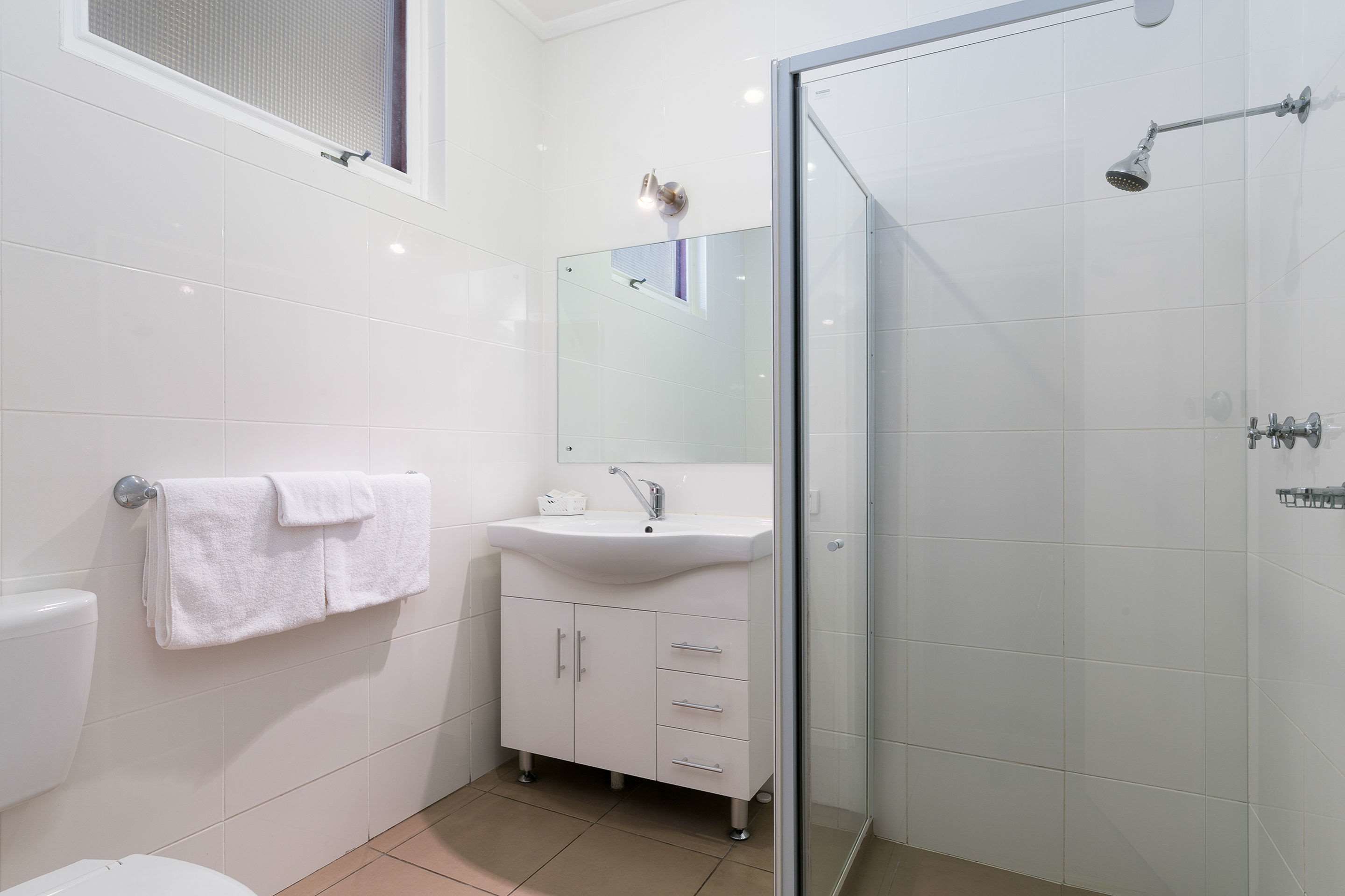 Une salle de bain moderne avec une douche à parois de verre, un lavabo blanc et un grand miroir au-dessus.