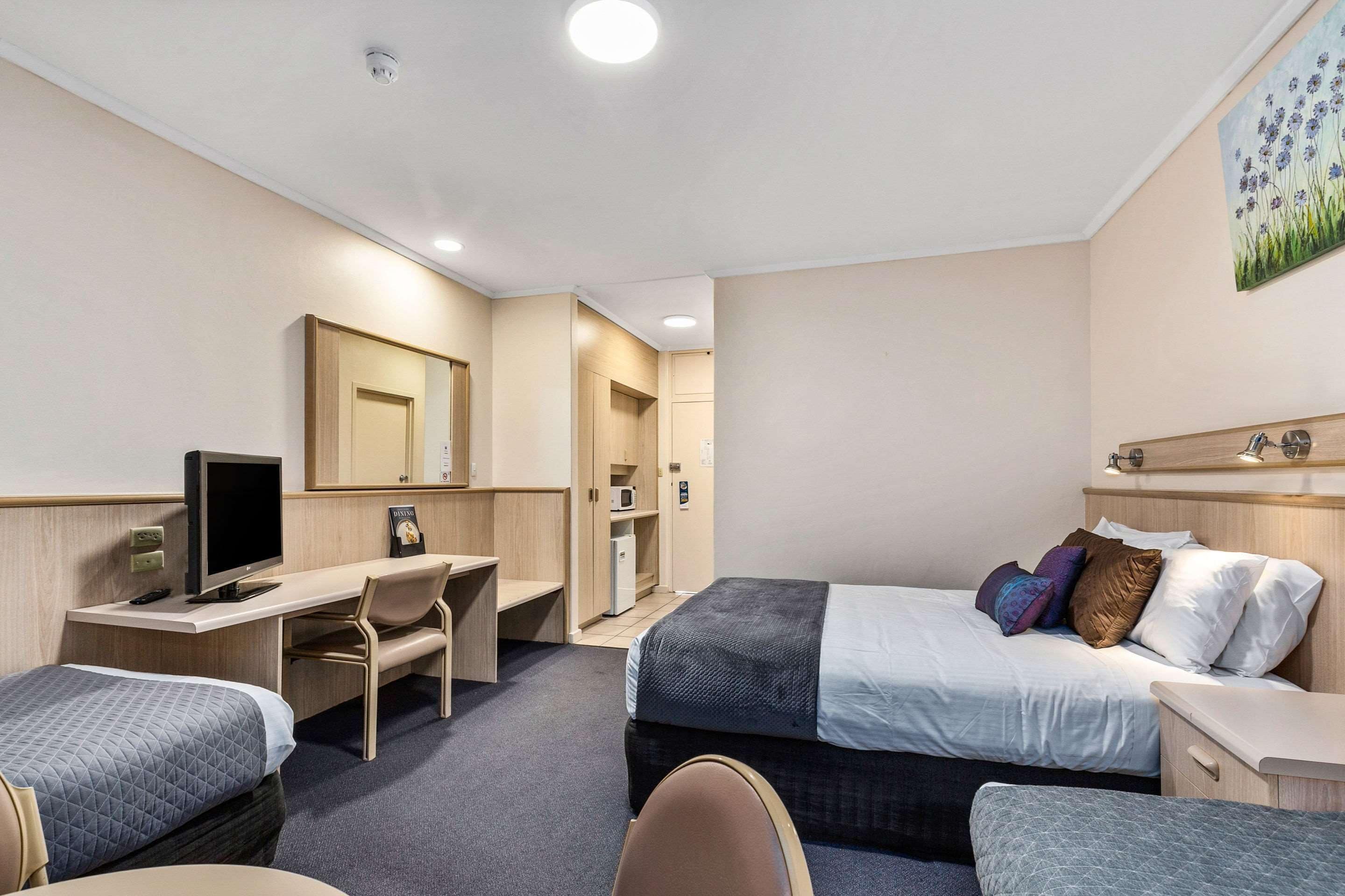 Habitación de hotel con cama, escritorio con computadora, silla, televisor pequeño y microondas.