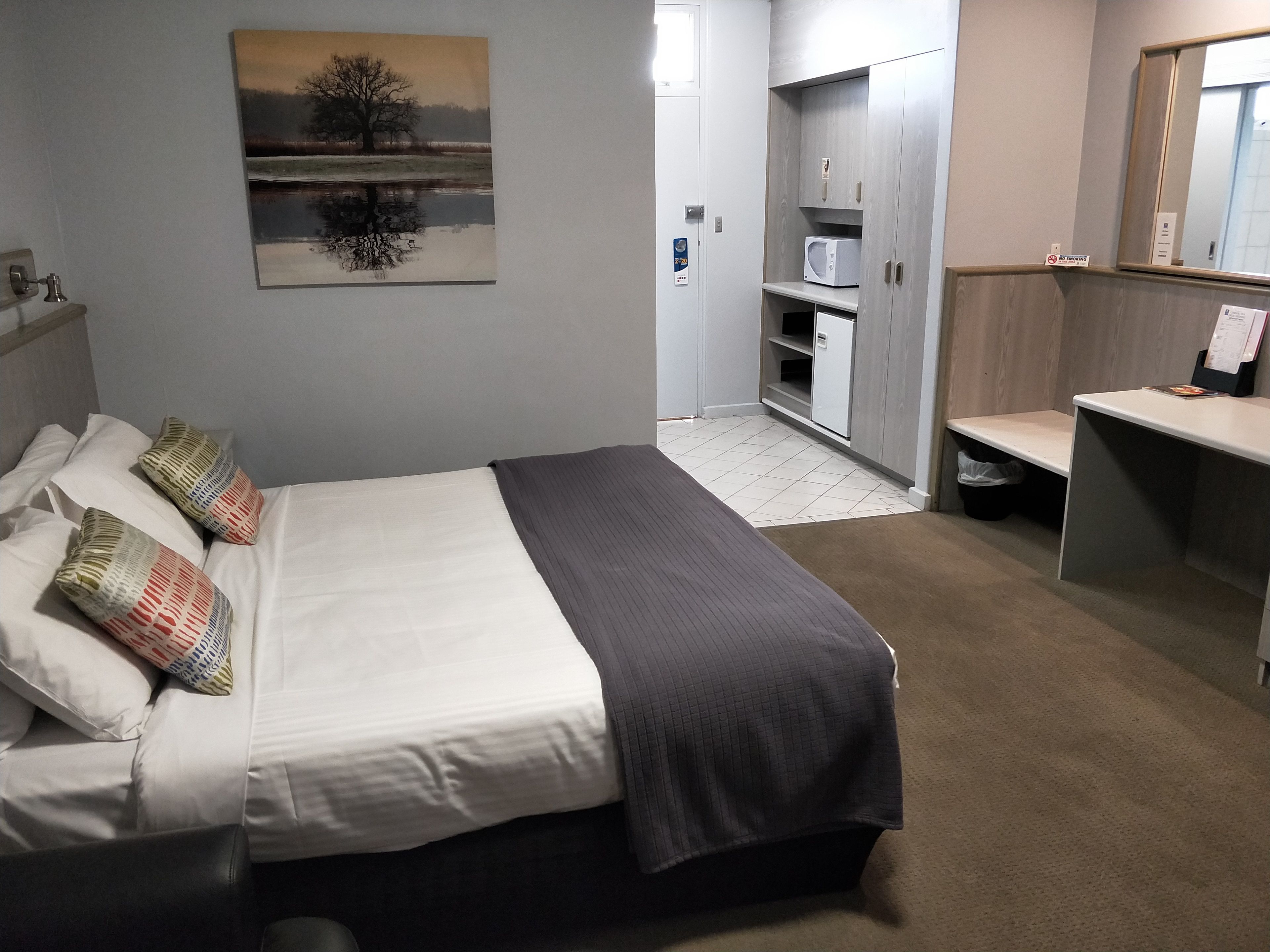 Quarto de hotel com cama, escrivaninha, micro-ondas e armário.