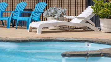 A pool area with lounge chairs, a potted plant, and a metal fence in the background.
