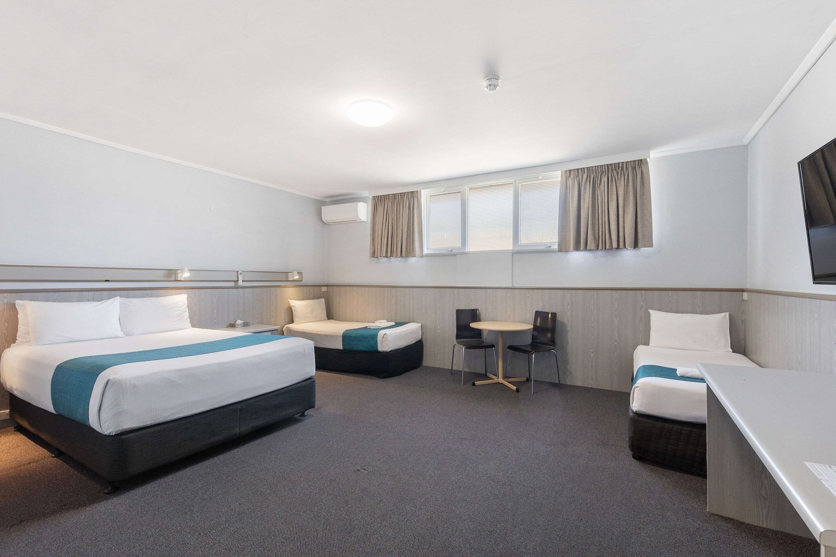 Habitación de hotel con dos camas, un escritorio, una silla y una mesita.
