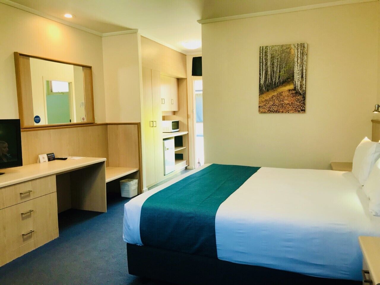 A hotel room with a bed, a desk, a mirror, and a painting on the wall.