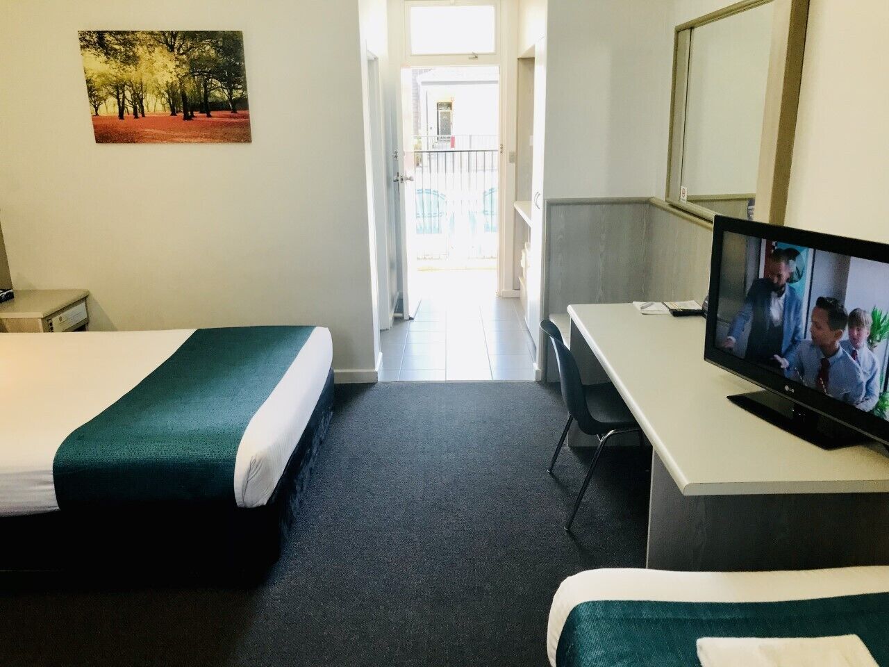 A hotel room with two single beds, a desk, a television, and a balcony view.