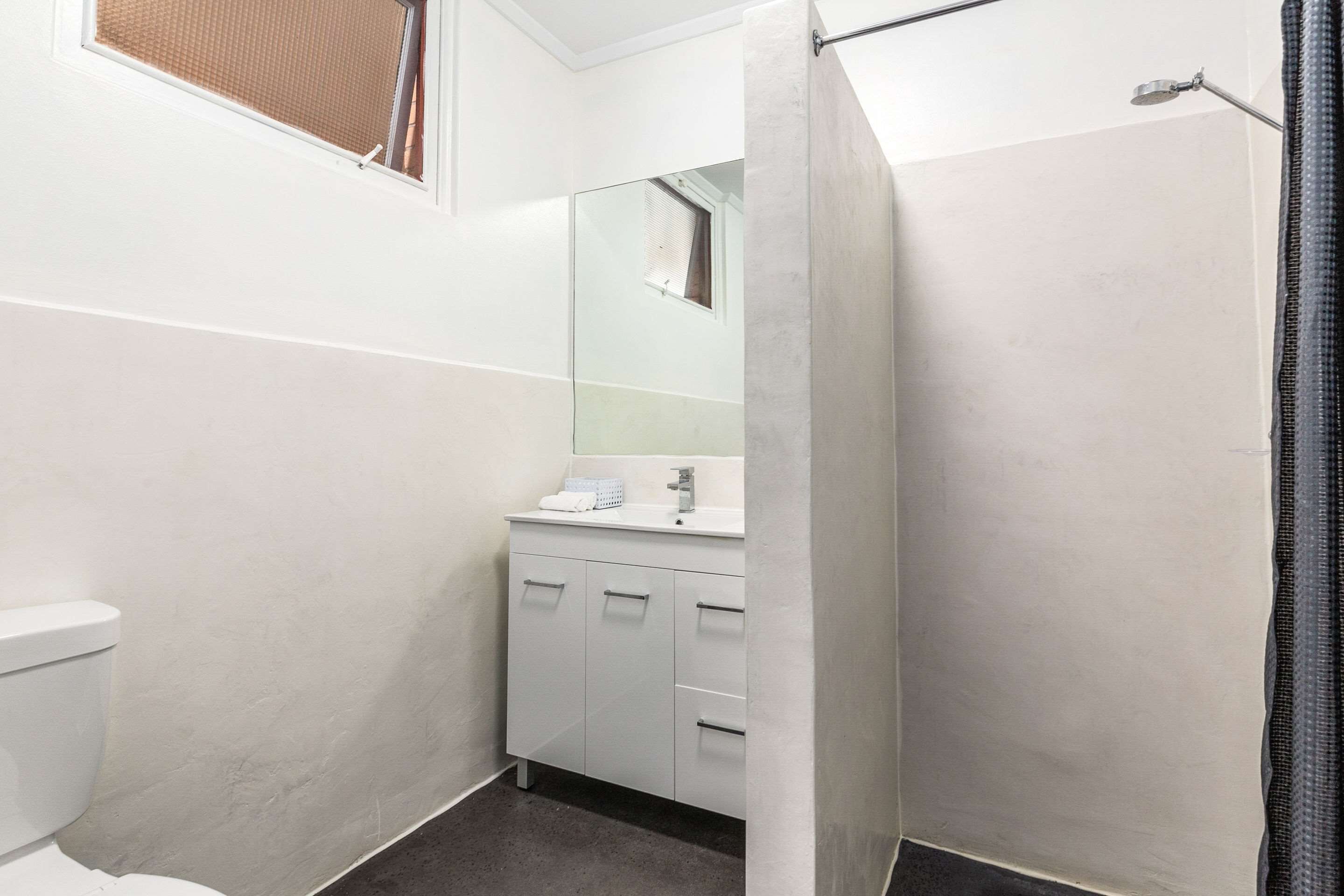 Un baño pequeño y moderno con inodoro, lavamanos con espejo y cabina de ducha.