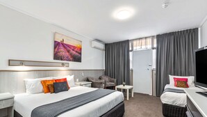 Une chambre d’hôtel avec un grand lit, un bureau, une chaise, une télévision et une fenêtre avec des rideaux.