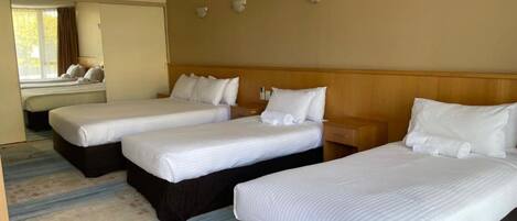 Une chambre d’hôtel avec trois lits simples, une tête de lit en bois, un grand miroir et une moquette à motifs.