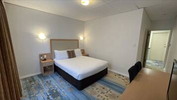 A hotel room with a large bed, bedside tables, a desk, and a patterned carpet.