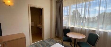 Habitación de hotel con cama, una pequeña mesa con dos sillas, un armario y un baño visible a través de una puerta abierta.