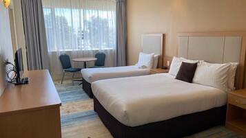 A hotel room with two beds, a desk, a chair, a small table, and a window with curtains.