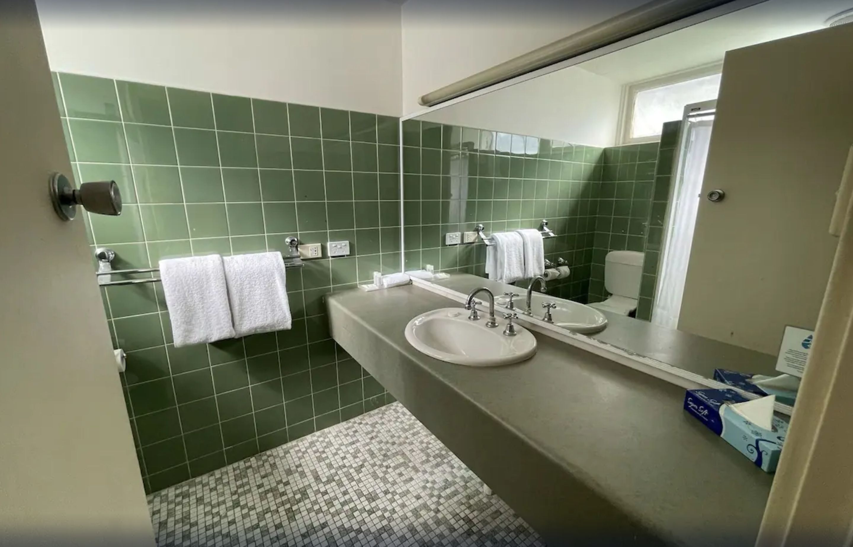 A bathroom with green tiled walls, a sink, a mirror, and two white towels hanging on hooks.
