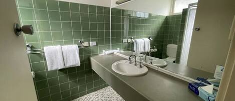 A bathroom with green tiled walls, a sink, a mirror, and two white towels hanging on hooks.