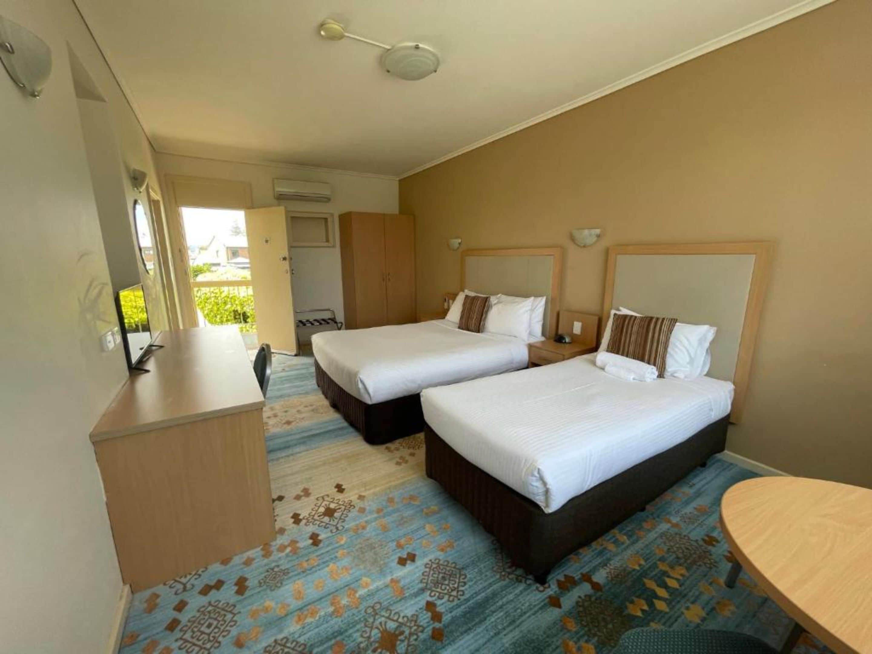 A hotel room with two beds, a desk, and a small round table.