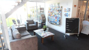 A hotel lobby with a staircase, seating area, and a wall with brochures. - Haven Marina Motel (Glenelg North)