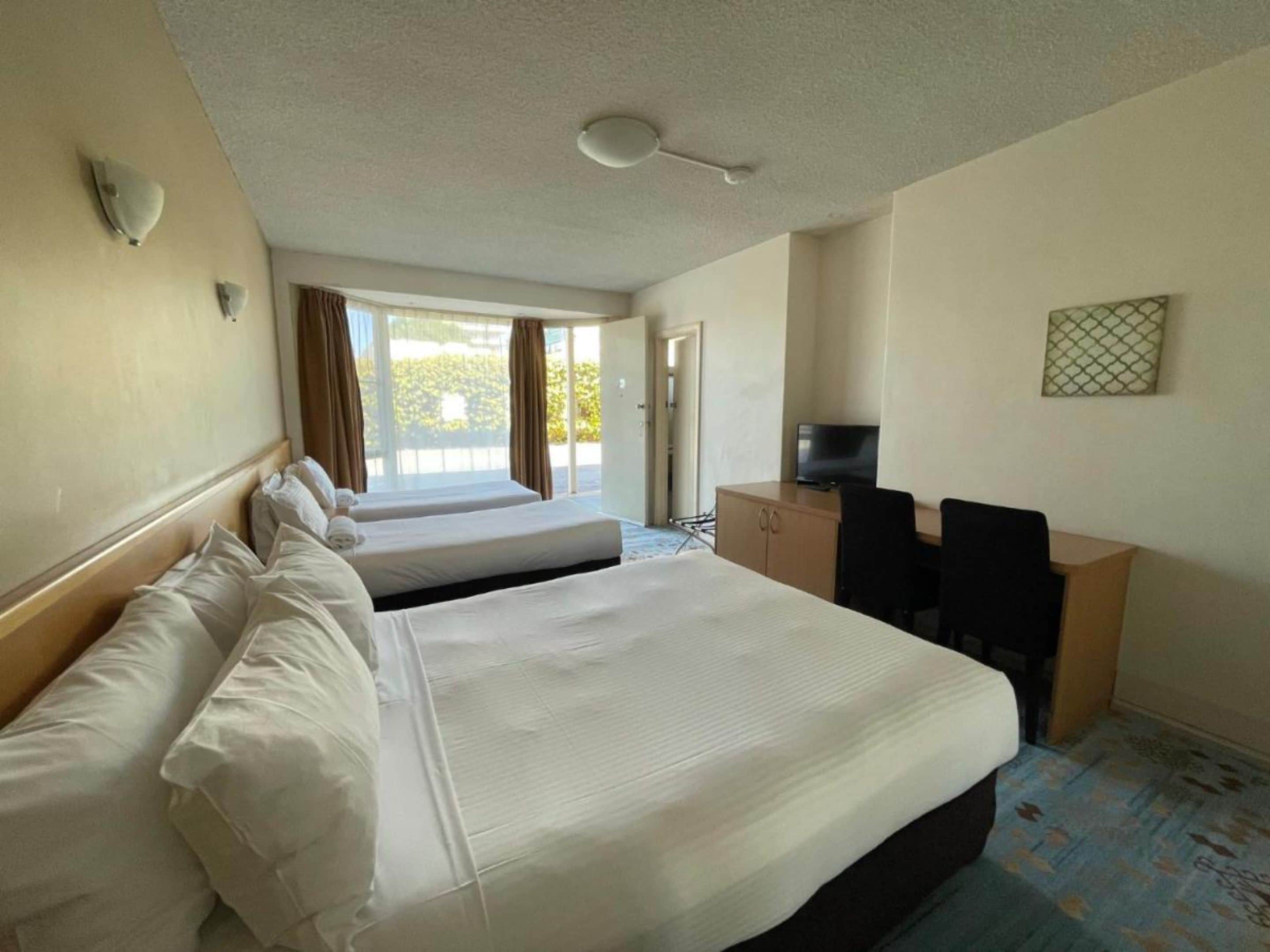 Une chambre d’hôtel avec deux lits, un bureau avec une chaise, une télévision et une fenêtre avec des rideaux.
