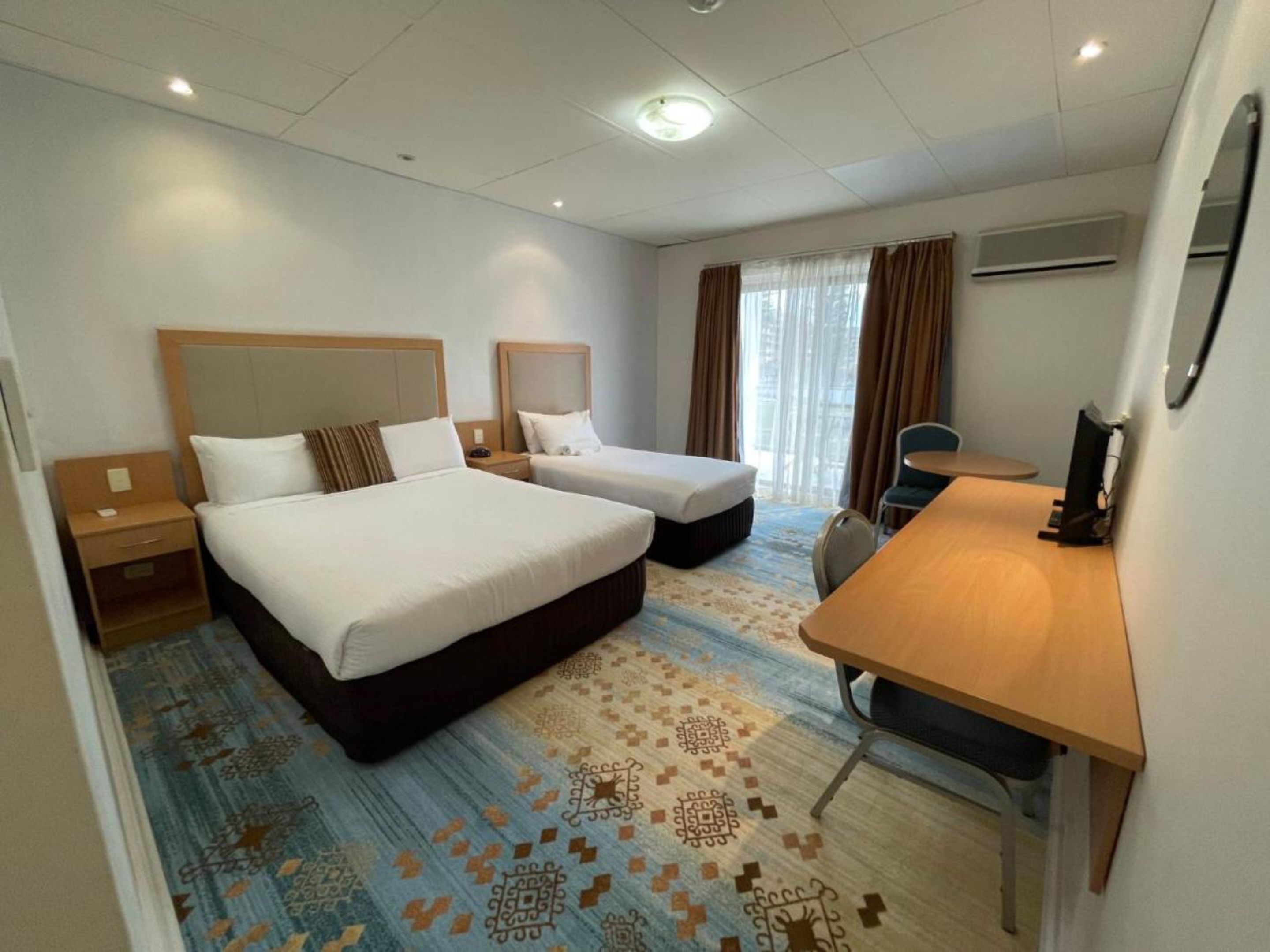 A hotel room with two beds, a desk, a chair, and a TV.