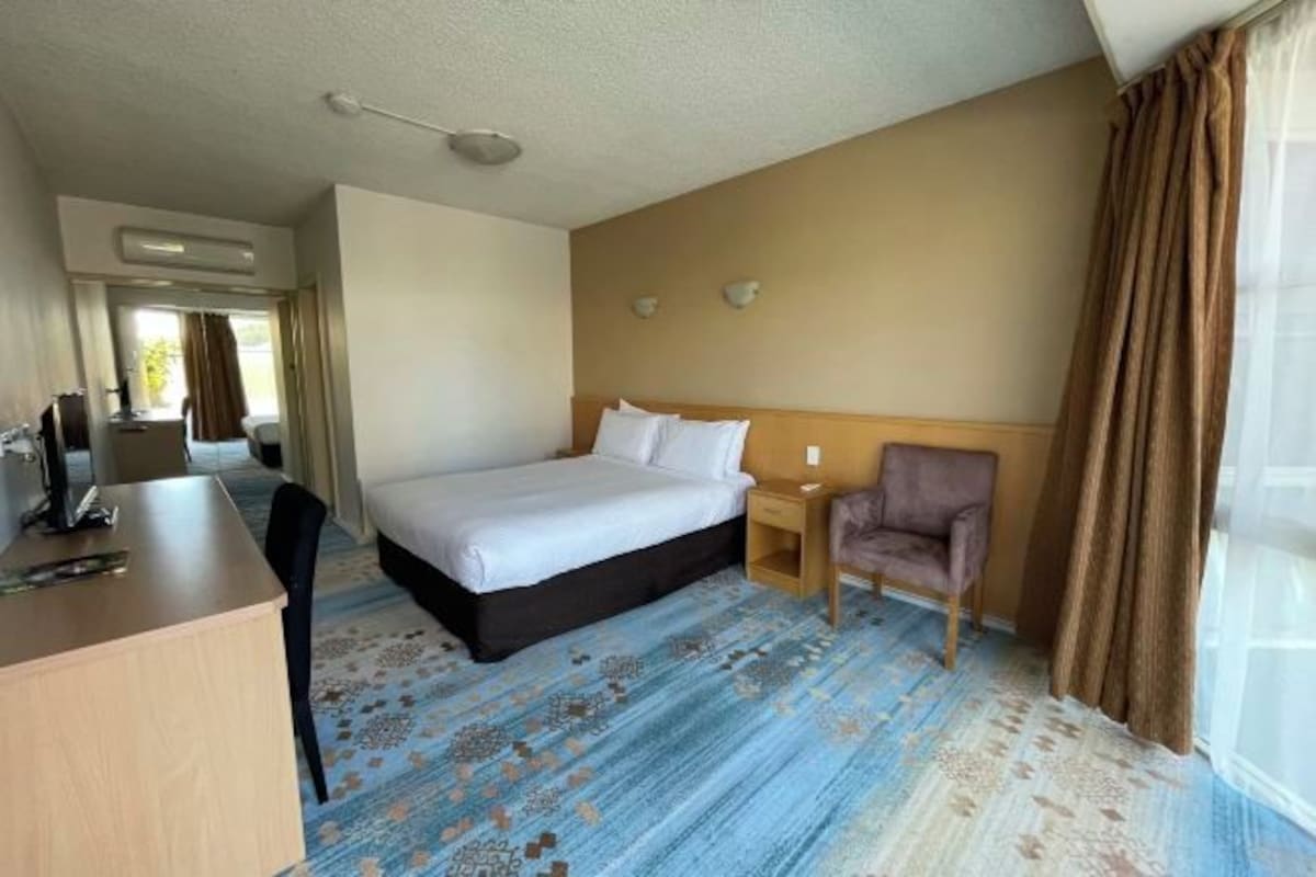 Une chambre d’hôtel équipée d’un lit, d’un bureau, d’une chaise, d’une table de chevet et d’une fenêtre avec des rideaux.