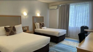 A hotel room with two beds, a desk, and a chair. There are wall-mounted lights and an air conditioning unit. - Haven Marina Motel (Glenelg North)