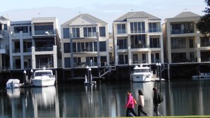 A waterfront residential building with multiple balconies, a marina with boats, and a grassy area in front. - Haven Marina Motel (Glenelg North)