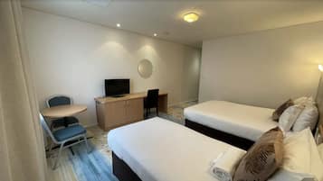 A hotel room with two single beds, a desk with a chair, a television, and a small table.