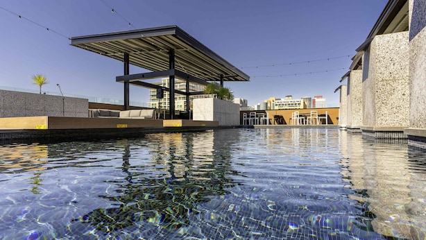 Una piscina cristalina con un área de descanso techada, paredes de piedra y luces colgantes.