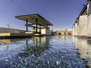 Una piscina cristalina con un área de descanso techada, paredes de piedra y luces colgantes.