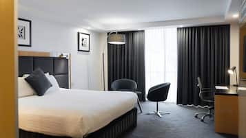 A modern hotel room with a large bed, a desk, a chair, and a large window with curtains.