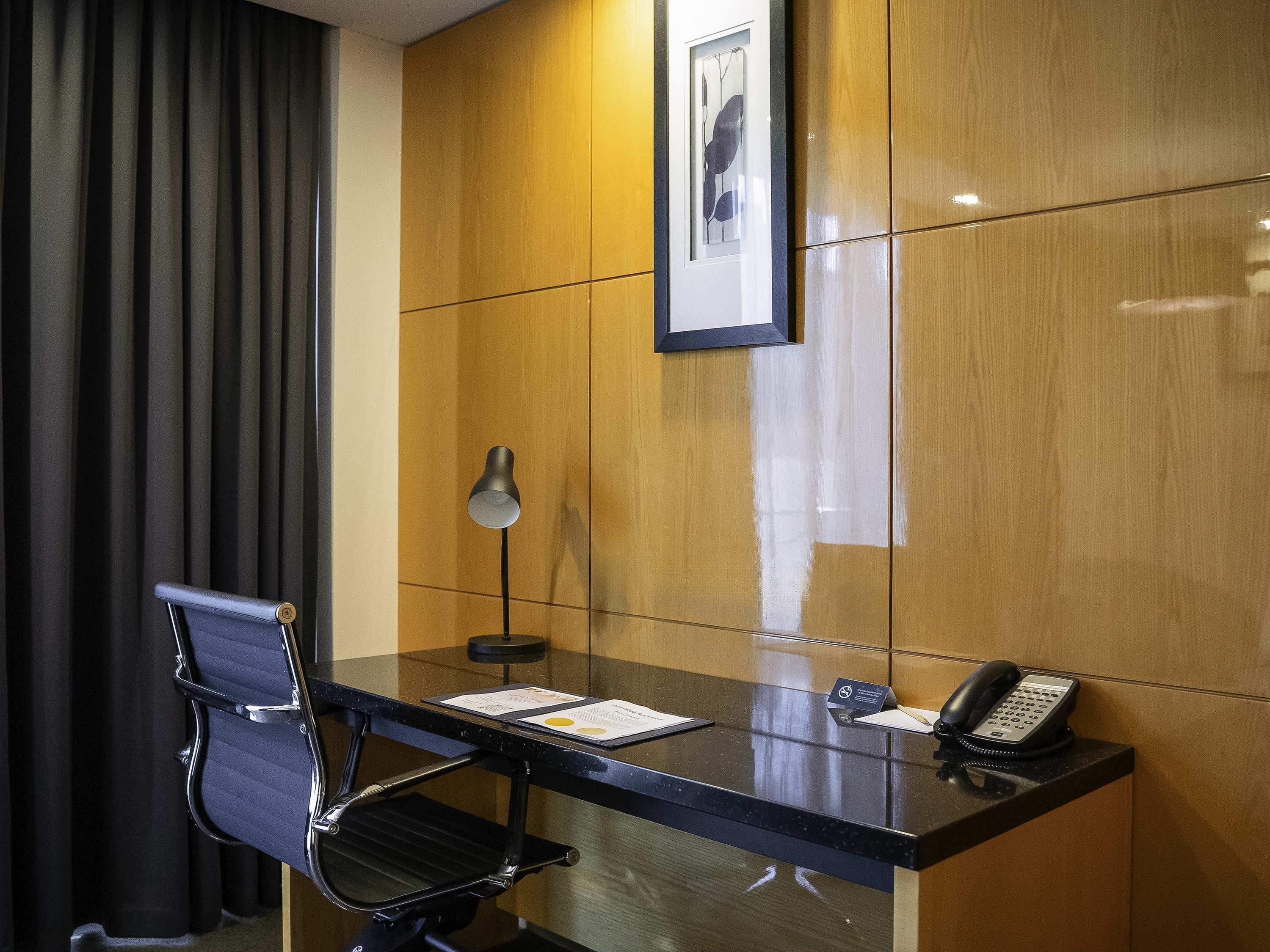 A hotel room with a desk, chair, telephone, and a framed picture on the wall.
